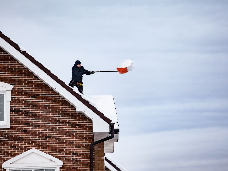 Les défis d'une bonne couverture de toiture quand il neige. Ici un couvreur qui entretient une toiture